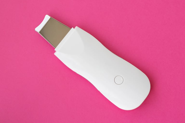 Elegant white ultrasonic skin scrubber with rose-gold accents and digital display on a pink surface
